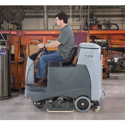 A Nilfisk BR755 Ride-on Floor Scrubber Dryer being operated in a warehouse.
