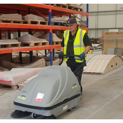 A Topfloor TF100-TRS Floor Sweeper being operated by a man in a warehouse.