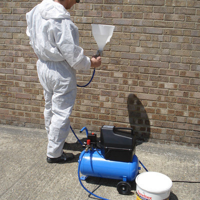 A Sandtex Hopper Spray Kit being used by a man in a white suit on an exterior wall.